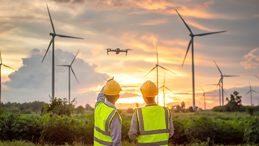 People in hardhats pointing at drone flying by windmills